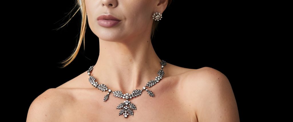 Close-up of a woman wearing an elegant vintage necklace and earrings from Dover Jewelry, featuring sparkling diamonds set in floral designs, highlighting the intricate craftsmanship of this one-of-a-kind piece.